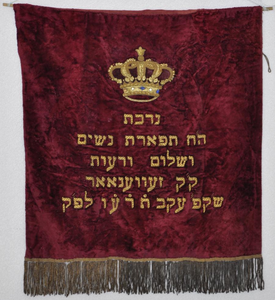 Rood fluwelen Thoramantel, met opschrift:  Nedobat  ha tephareth nosjim wesjaloom werowoth kk Zevenaar sj(abbat) k(oudesh) akow tod or lepok. Vertaling: Geschenk van de Vereniging Sieraad van de vrouwen en vrede en vriendschap heilige gemeente Zevenaar sabbath in het jaar 5676 (1916)